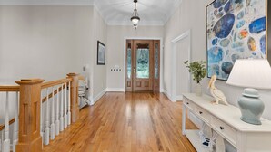 A hallway with wooden flooring, a white console table with decorative items, and a large abstract painting on the wall. - Sunset Pointe by AvantStay | Waterfront, Beach, Fire Pit | Sleeps 14 | 5BDR 4BA (Troutman)