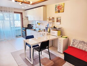 Une cuisine moderne avec des meubles blancs, une table à manger avec des chaises, un four à micro-ondes et un canapé rouge.