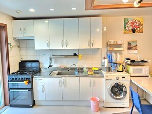 Une cuisine avec des meubles blancs, une cuisinière à gaz, un four à micro-ondes, un lave-linge et un évier.