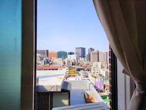Une vue sur le paysage urbain, prise depuis une fenêtre dont le rideau est partiellement tiré.