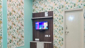 Et værelse med teal vægge, et blomstret tapetmønster, et tv-skab i træ med et fladskærms-tv, en hvid dør og en loftsvifte.