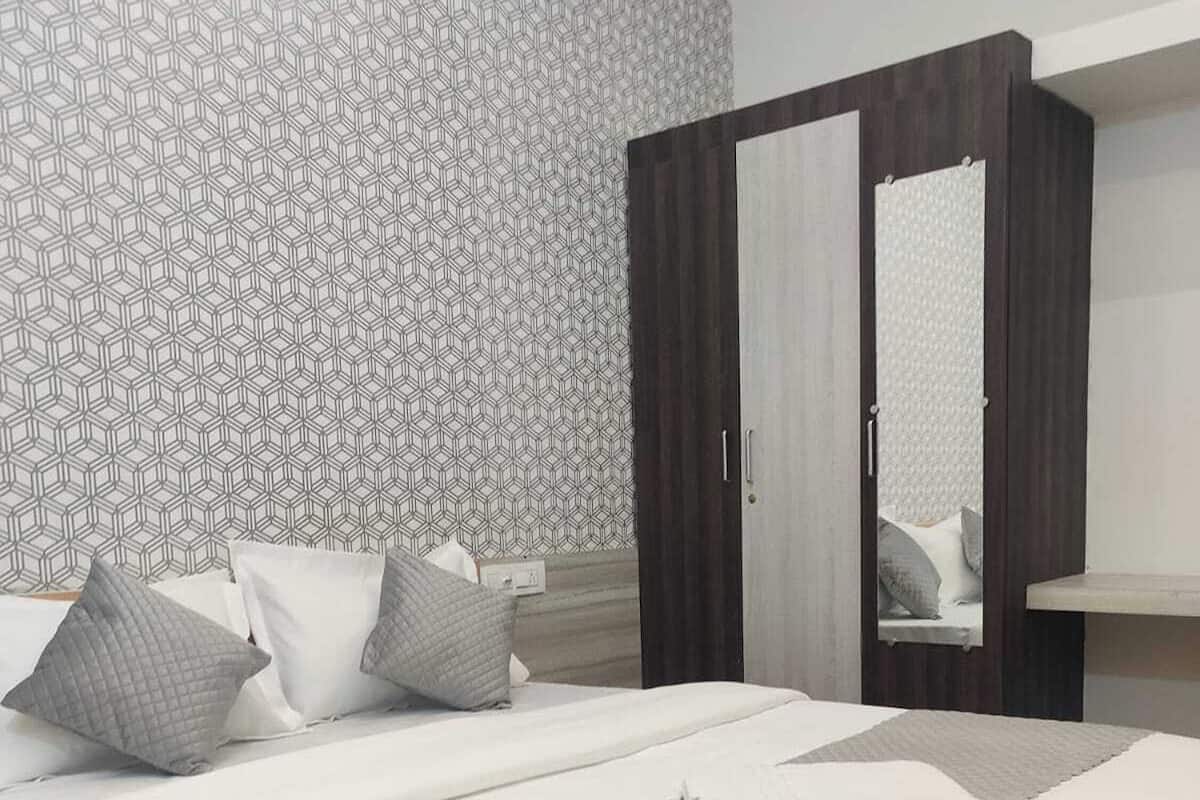 A modern bedroom with a geometric patterned wallpaper, a bed with grey bedding and pillows, a wooden wardrobe, and a mirror on the wardrobe door.