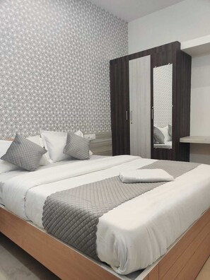 A modern bedroom with a geometric patterned wallpaper, a bed with grey bedding and pillows, a wooden wardrobe, and a mirror on the wardrobe door. - VILASINI INN BTM Layout, Bengaluru (Bengaluru)