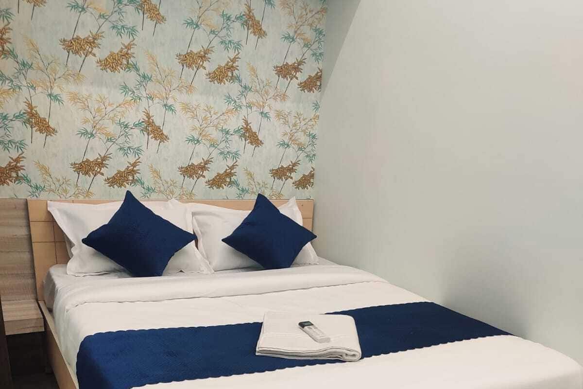 A neatly made bed with white and blue bedding, a blue throw blanket, and a folded towel on the bed.