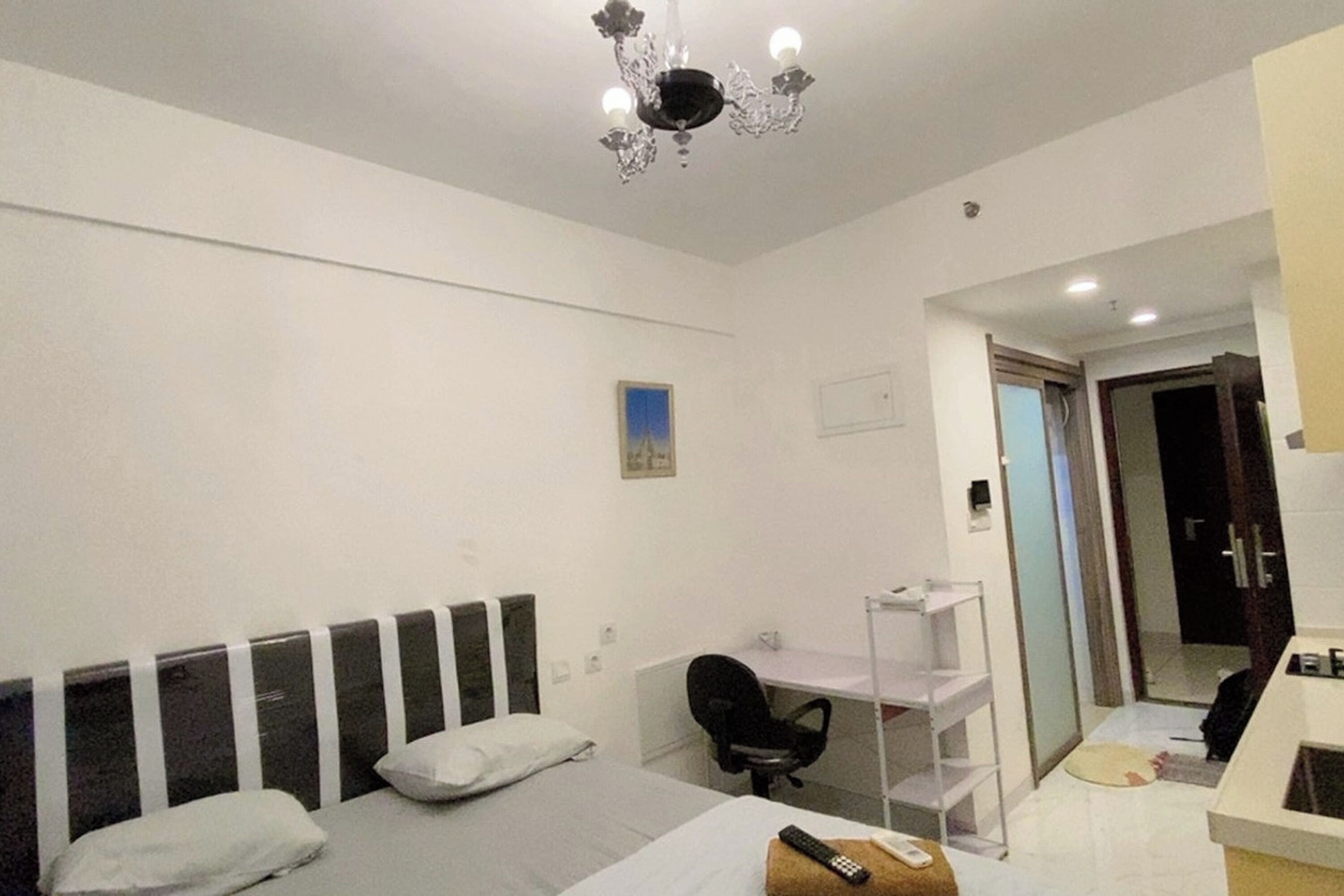 A hotel room with a bed, a desk, a chair, a small sink, and a mirror.