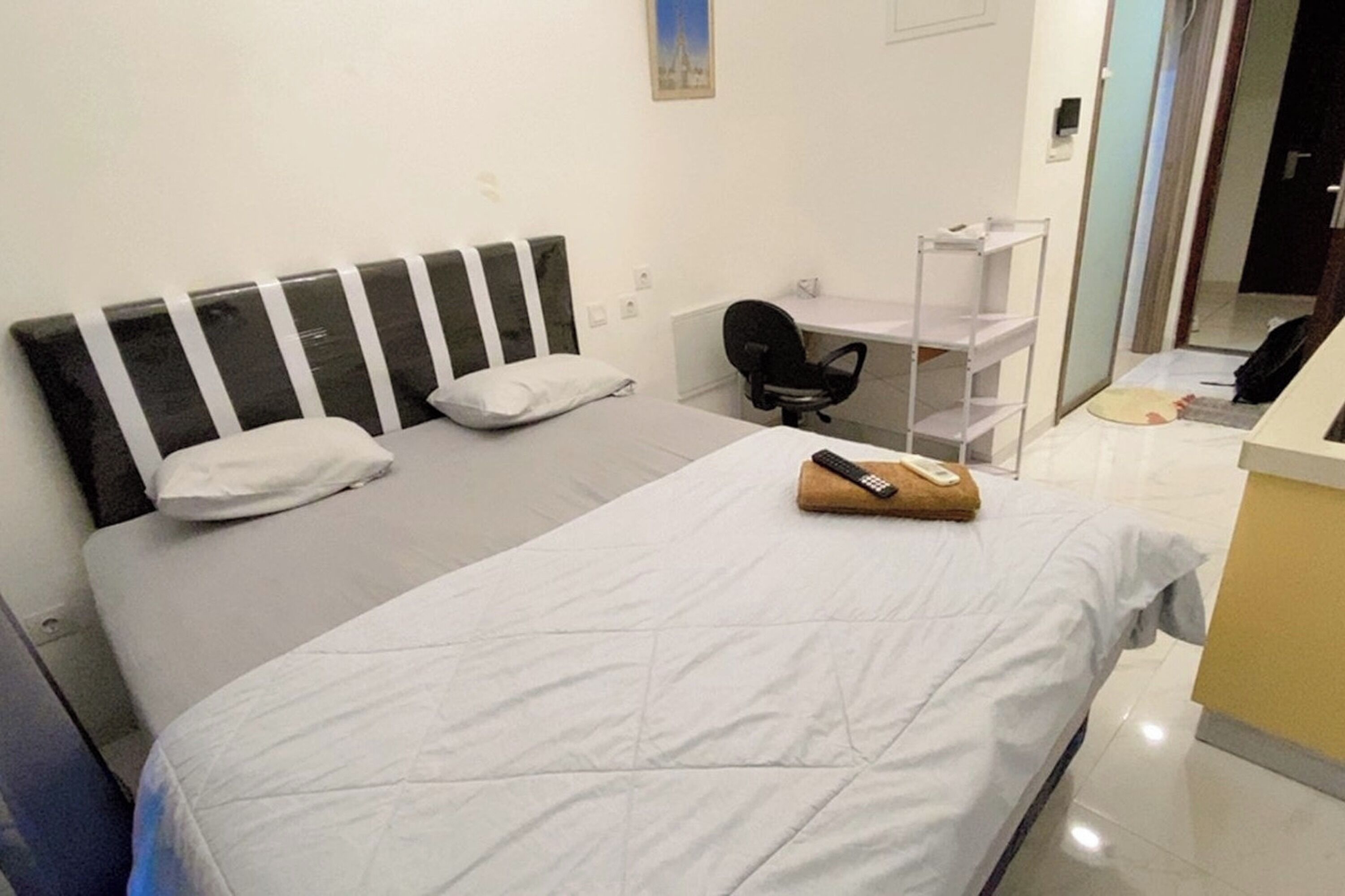 A neatly made bed with pillows, a bedside chair, and a desk with a chair.