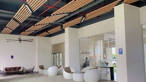 A modern lobby with a high ceiling, wooden slats, and a seating area with white chairs and a sofa. - Sky House Bsd By Mizu Rooms (Pagedangan)
