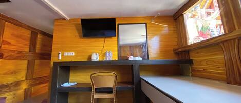 Een kamer met een houten wandpaneel, een flatscreen-tv boven een bureau, een stoel en een raam met uitzicht op een glas-in-loodwerk.