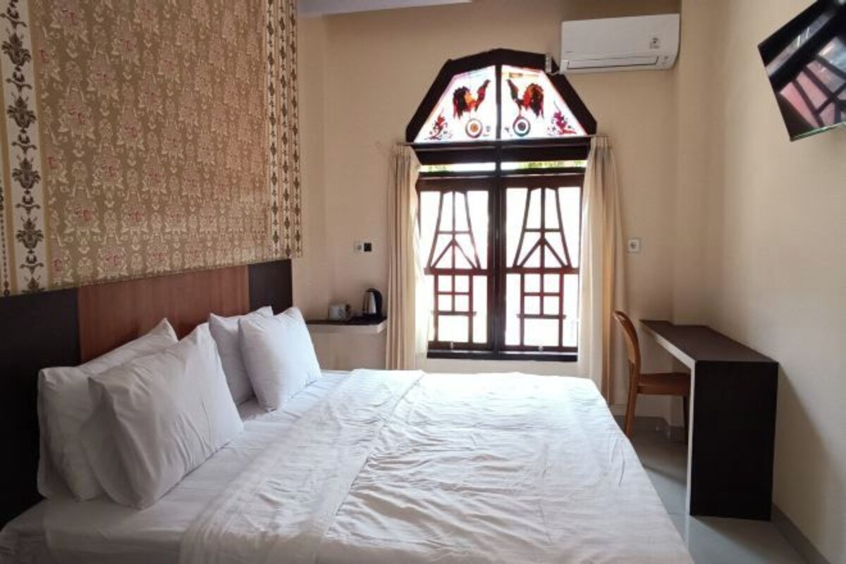 Une chambre d’hôtel comprenant un lit, un bureau, une chaise et une fenêtre ornée d’un motif décoratif.