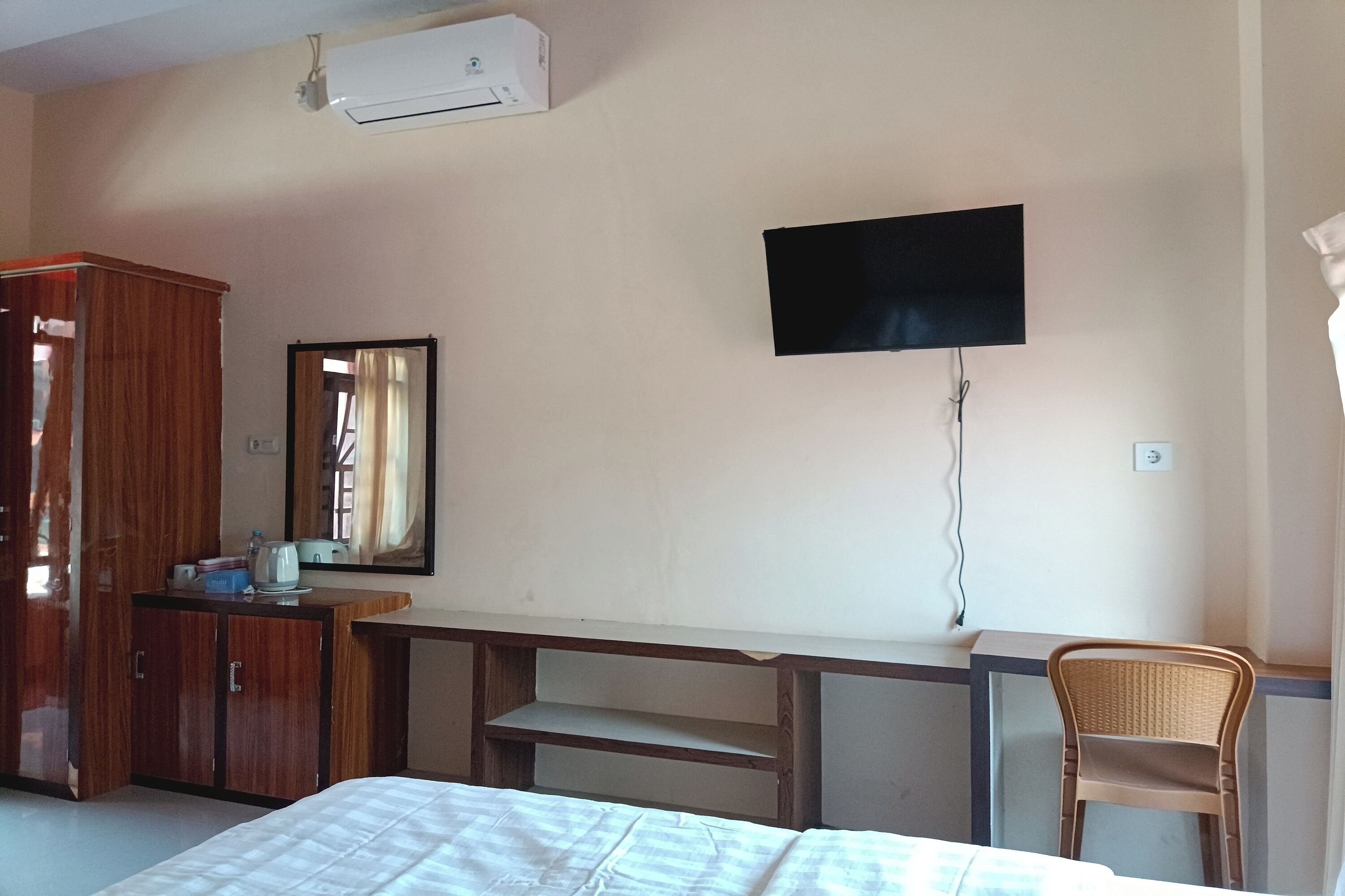 Habitación de hotel con cama, armario de madera, escritorio, silla y televisor montado.