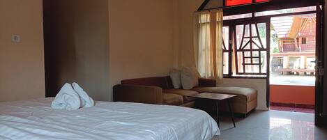 A hotel room with a large bed, a sofa, a small table, and a view of the outside through a window.
