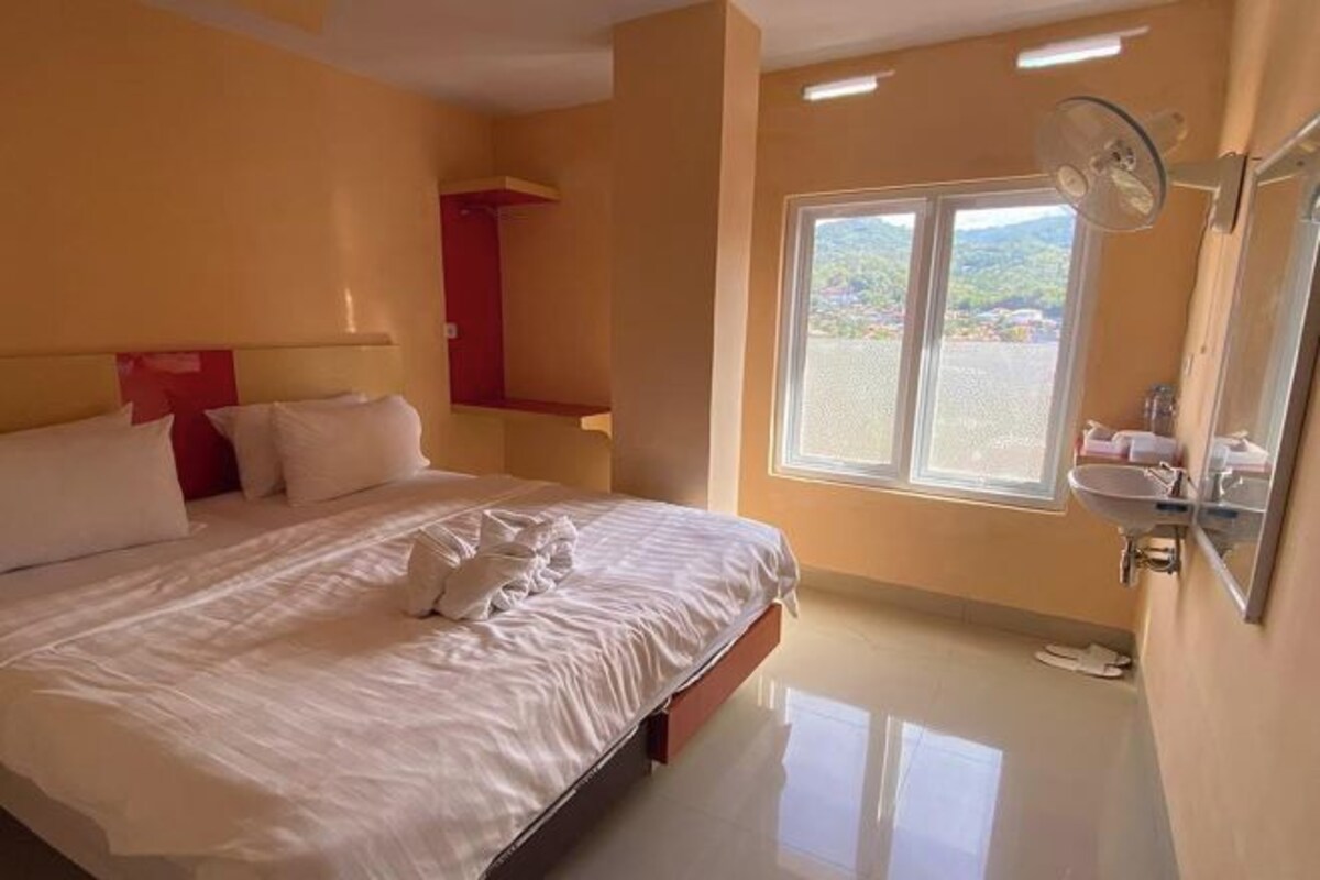 Une chambre d’hôtel avec un lit, une fenêtre, un lavabo et un miroir.