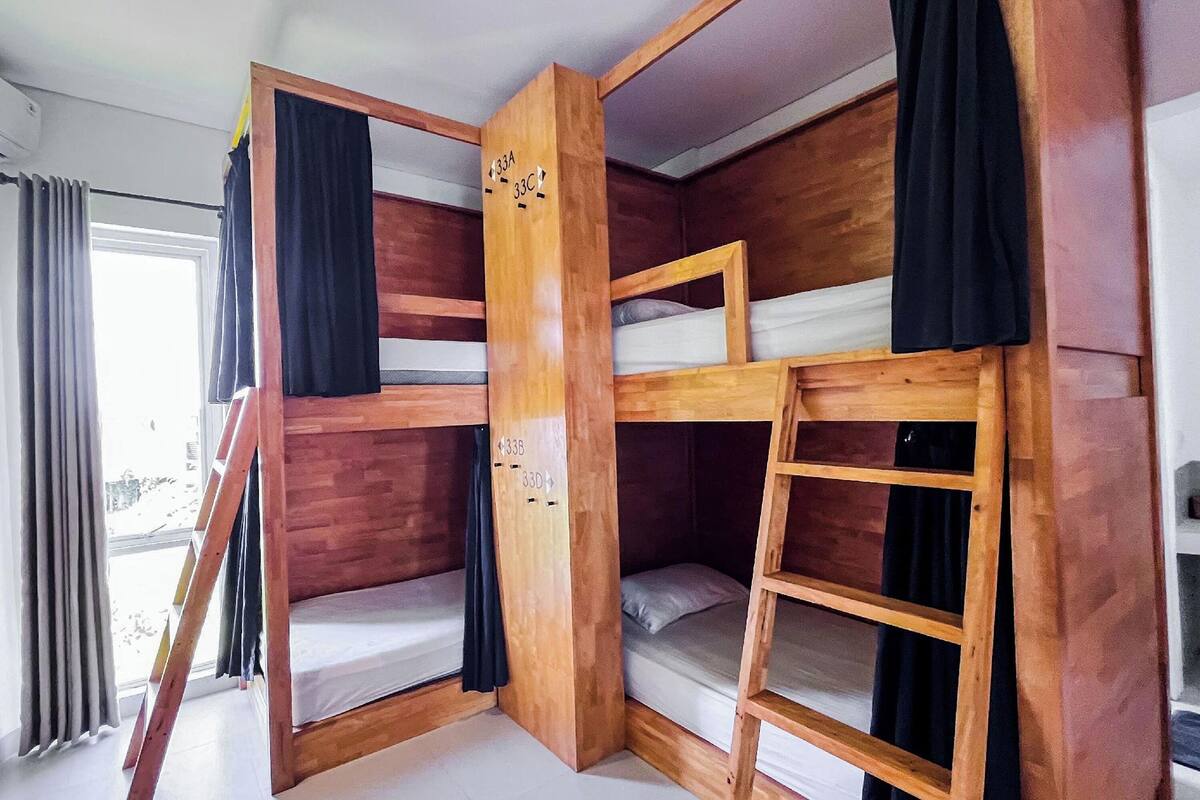 Une chambre avec des lits superposés, une échelle en bois et une fenêtre avec des rideaux.