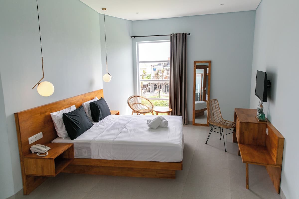 Une chambre d’hôtel moderne avec un lit en bois, une table de chevet avec un téléphone, une chaise, une petite table, un téléviseur et une vue sur l’extérieur.