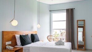 A modern bedroom with a wooden bed, bedside tables, a hanging light fixture, a large window with curtains, and a mirror. - Coco & Pineapple Pants Hostel (Canggu)
