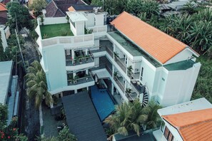 A multi-story building with a swimming pool, balconies, and surrounding greenery. - Coco & Pineapple Pants Hostel (Canggu)
