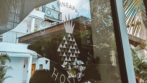 A glass door with a reflection of a building labeled "Pineapple Hostels" and a palm tree. - Coco & Pineapple Pants Hostel (Canggu)
