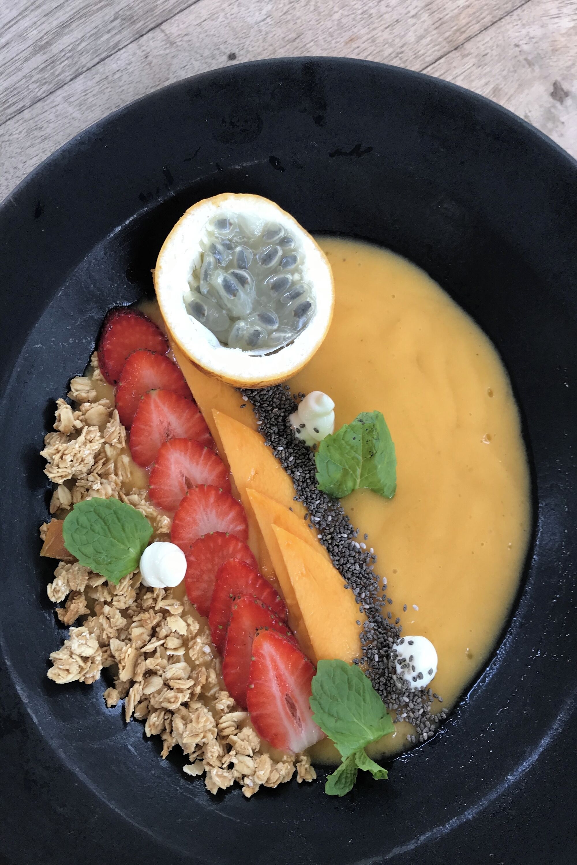 Eine Schüssel mit Obst und Granola, dazu ein Mangostreifen, Erdbeeren und Chiasamen.