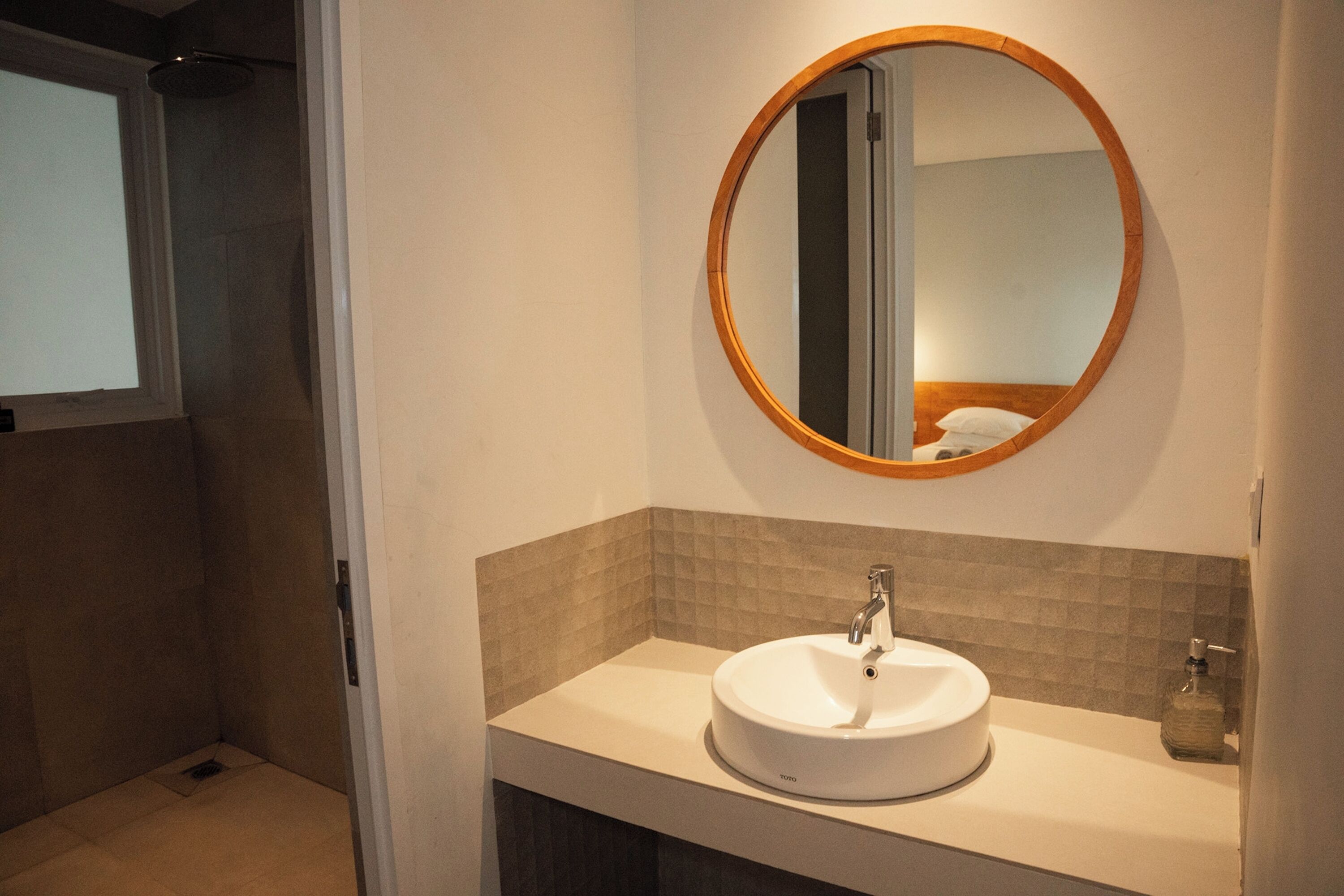 A bathroom with a round mirror, a sink, and a shower area.