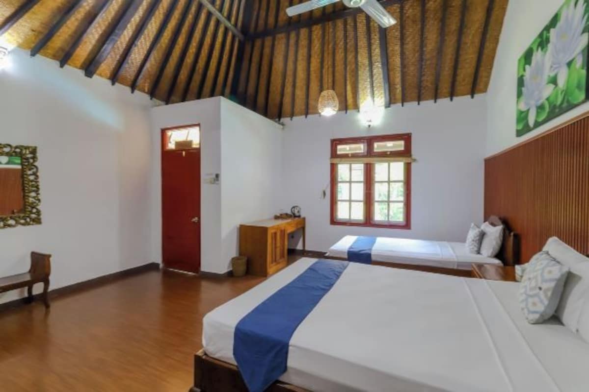 Una habitación con dos camas, un escritorio de madera, una puerta roja y un ventilador de techo.