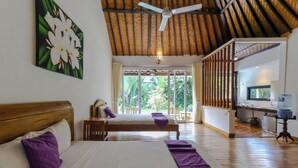Un dormitorio con dos camas, ventilador de techo y vista al jardín.
