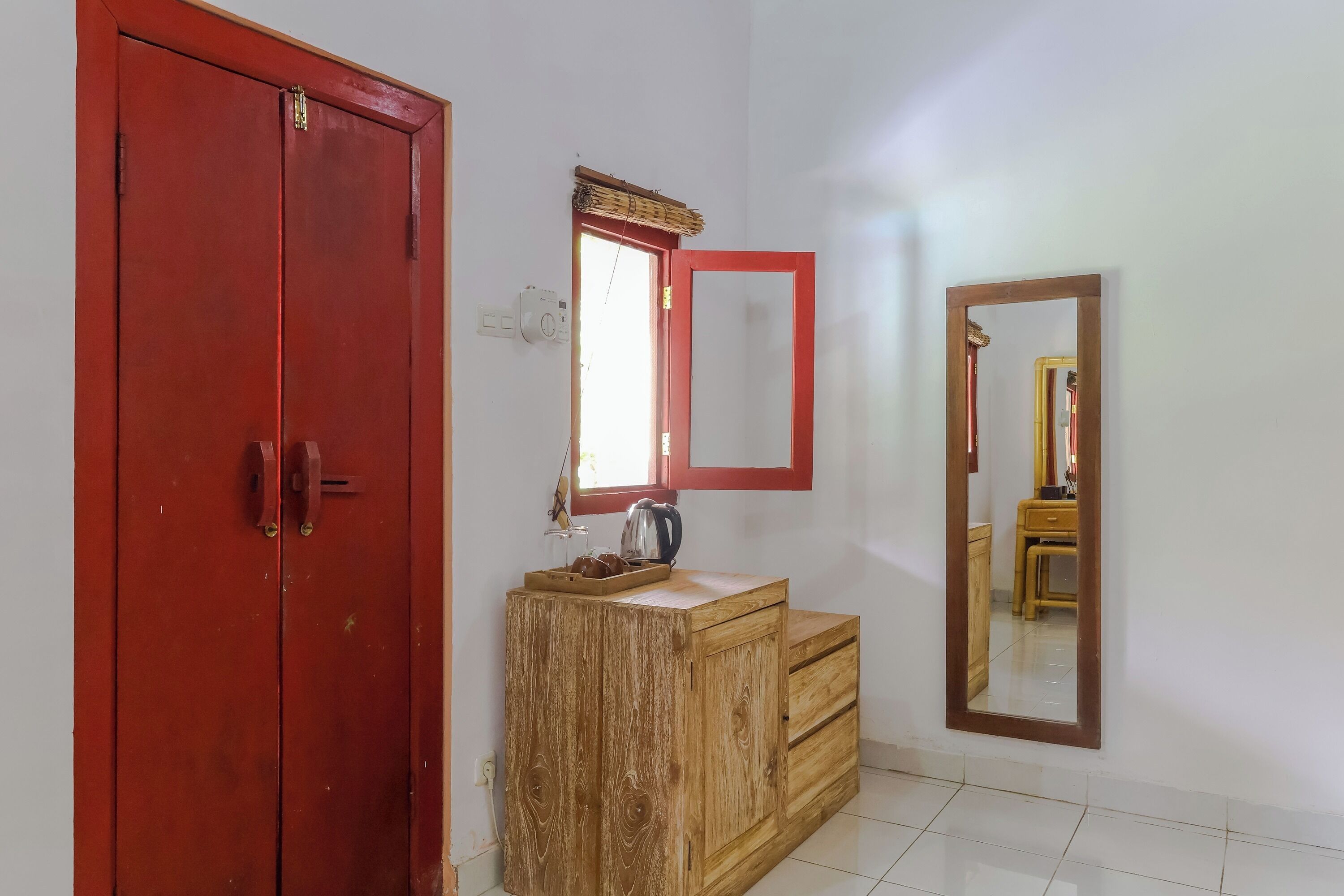 Une pièce avec un meuble en bois, une porte rouge, un miroir et une fenêtre dotée d’un cadre rouge.