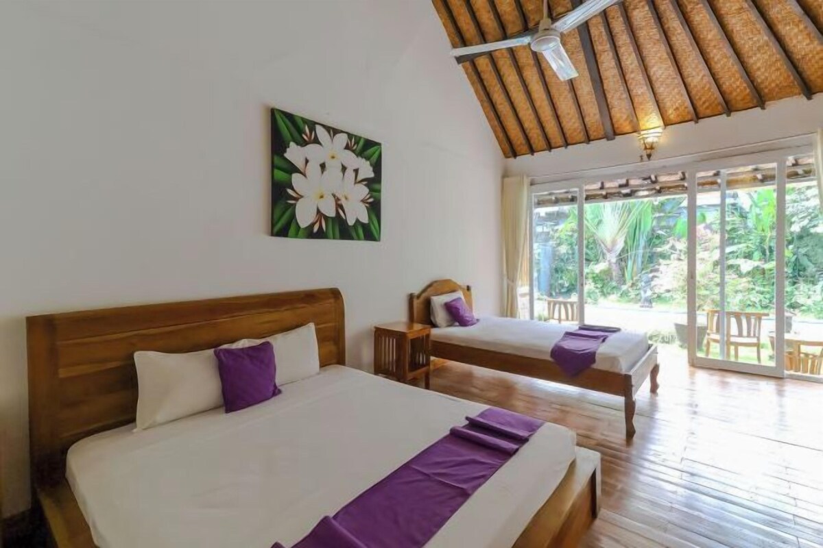 Una habitación con dos camas de madera, un ventilador de techo y un amplio ventanal con vistas a la vegetación.