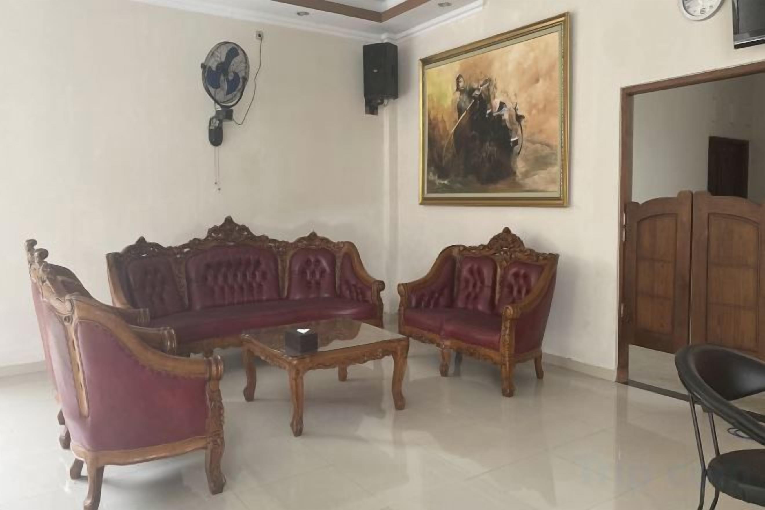 A room with two red upholstered sofas, a wooden coffee table, a wall-mounted fan, and a painting.