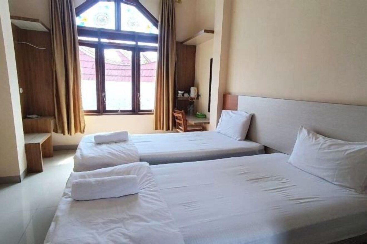 A hotel room with two beds, a desk, and a window with curtains.