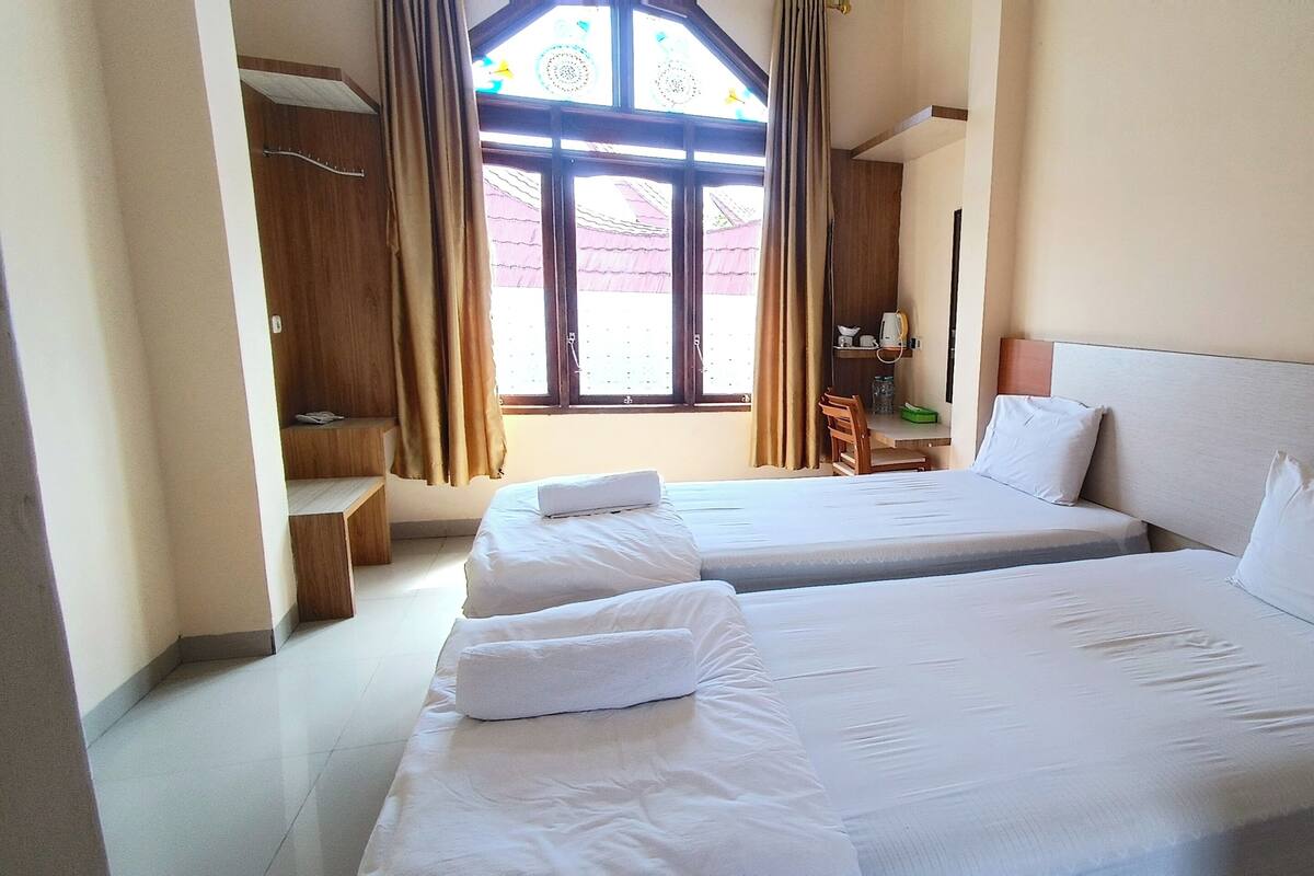 Une chambre d’hôtel avec deux lits, un bureau en bois, une chaise et une fenêtre avec des rideaux.