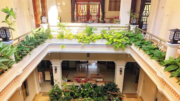 Um saguão de hotel com uma escadaria central, entrada decorativa e área de estar com vista para o interior.