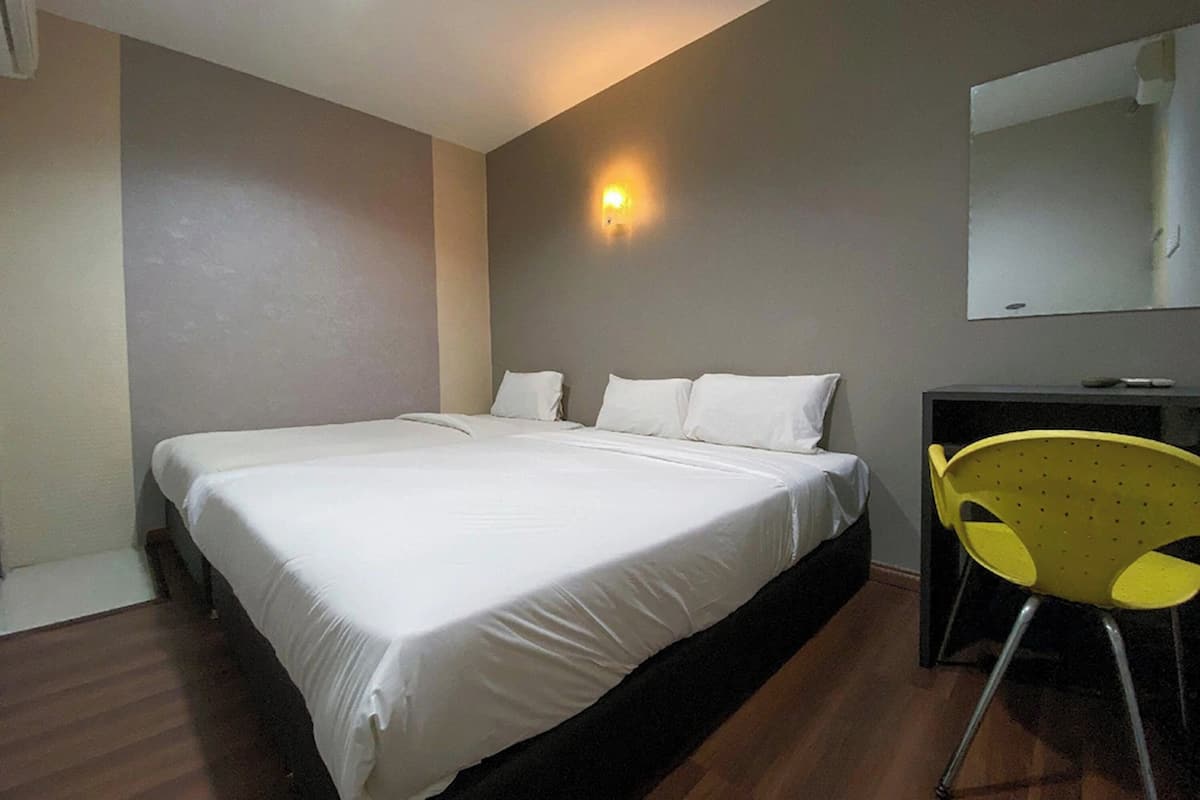 A bedroom with a large bed, a desk, a chair, and a wall-mounted light.