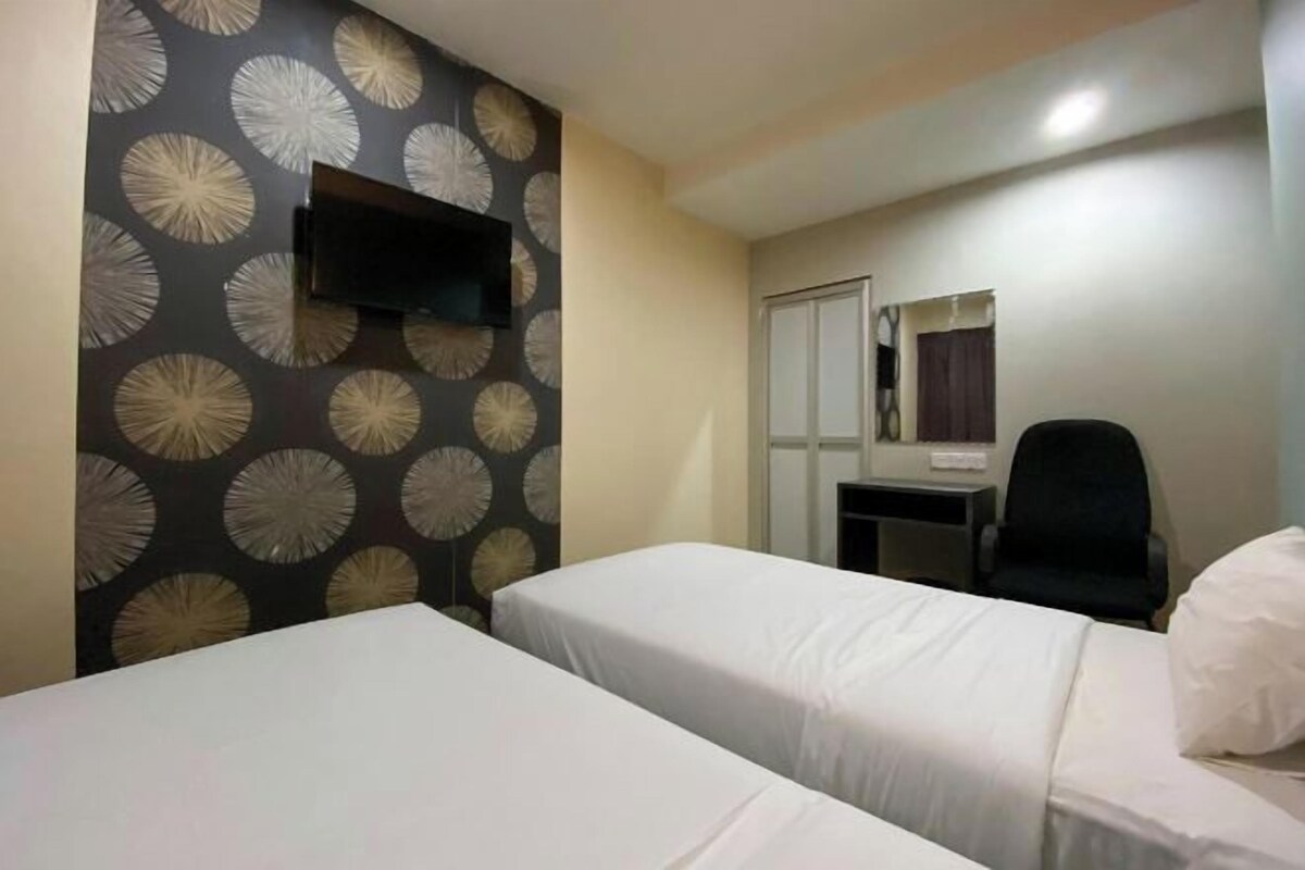 A hotel room with two beds, a desk, a chair, a TV mounted on the wall, and a mirror.
