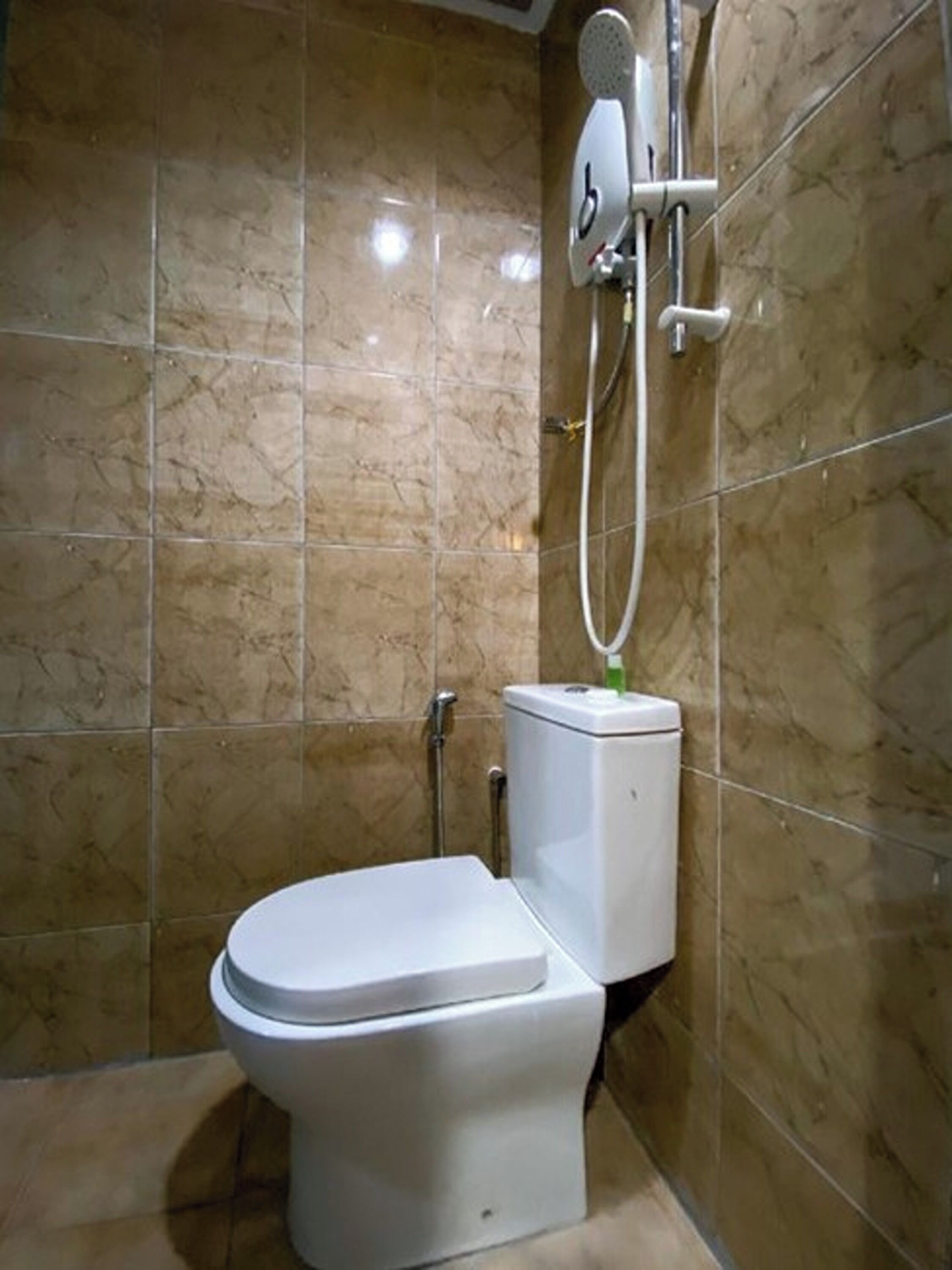 A bathroom with a toilet, a shower unit, and a marble-tiled wall.
