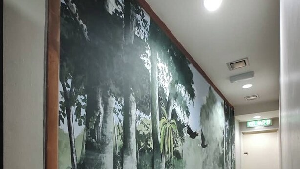 Un pasillo con un mural de una escena de bosque, piso de madera y una puerta con la leyenda 'EXIT'.