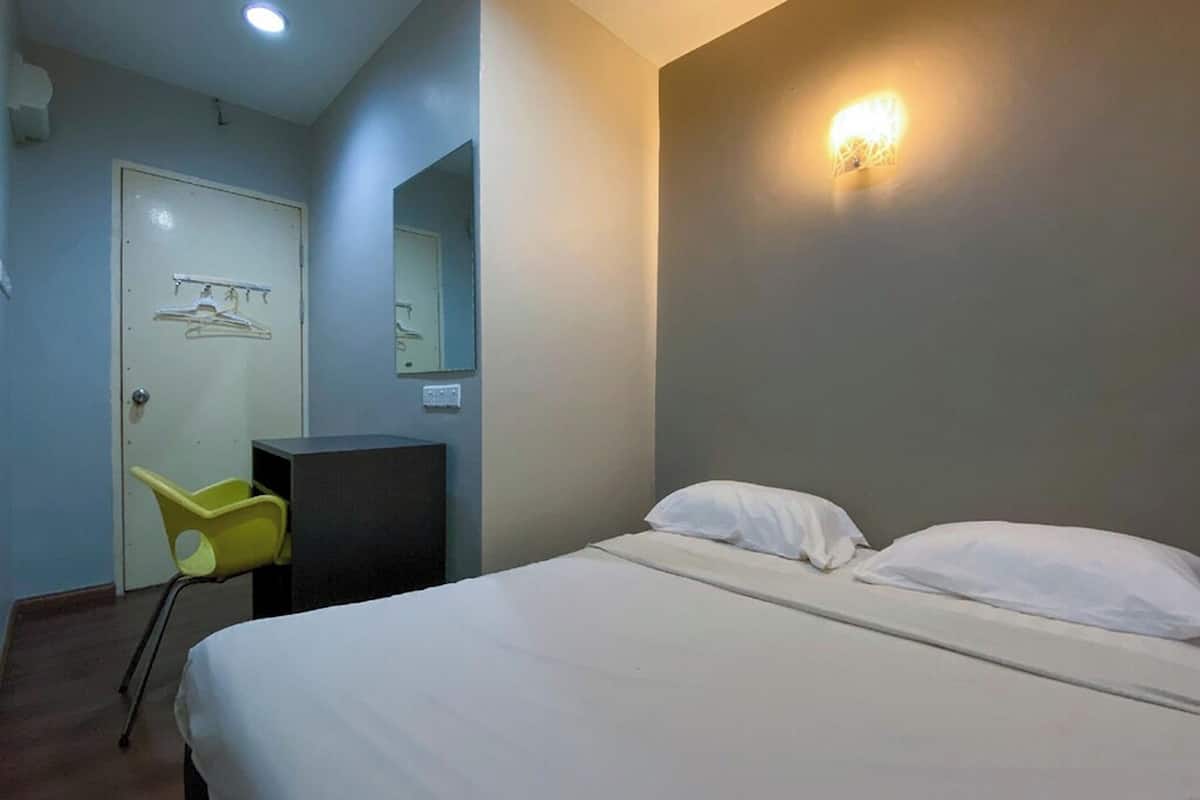 A hotel room with a bed, a desk, a chair, a wardrobe, and a mirror.