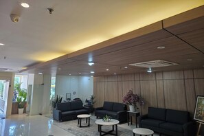Un hall d’entrée moderne avec un comptoir d’accueil, des canapés noirs et une grande plante en pot.
