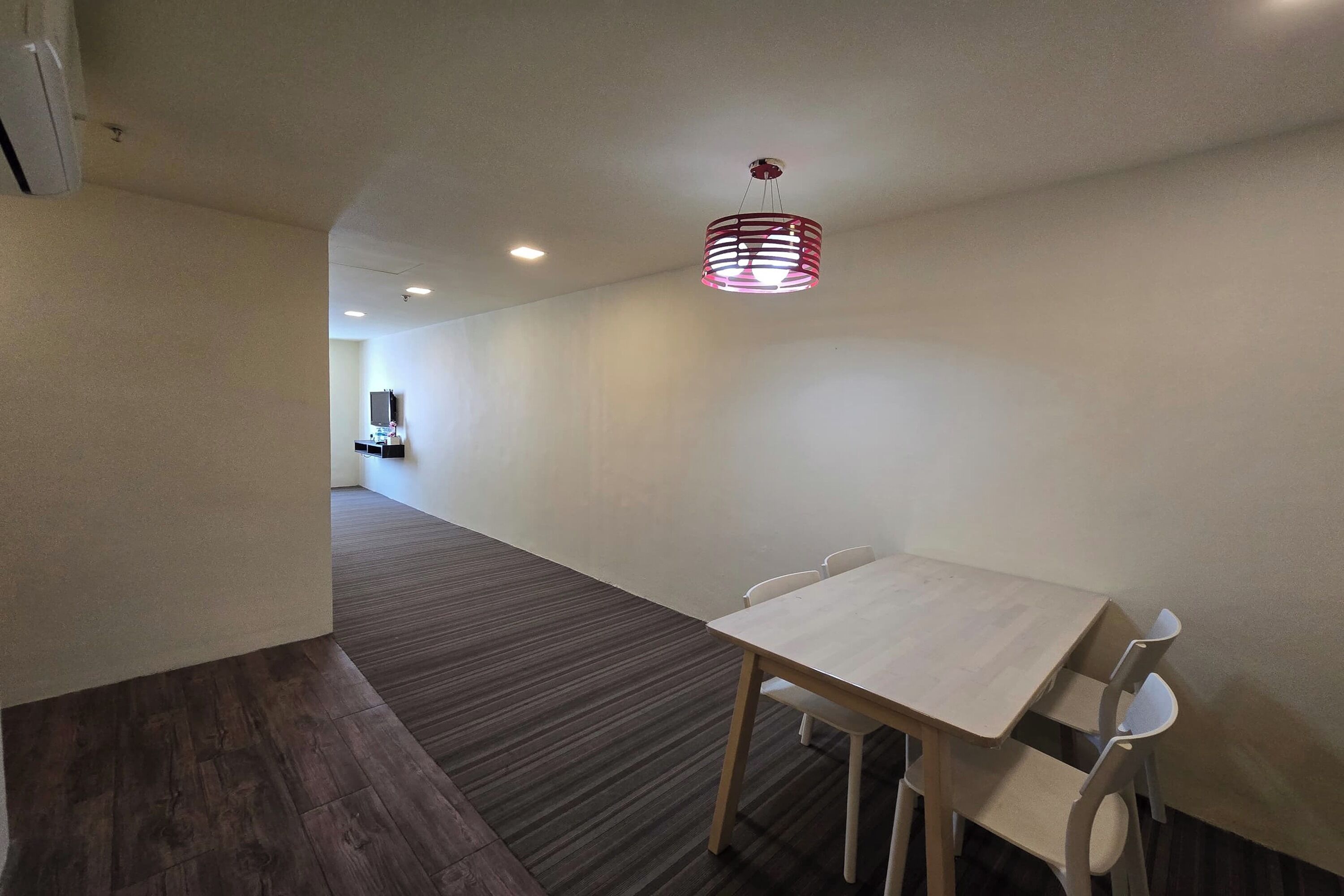 A modern hotel room with a wooden table and chairs, a patterned carpet, and a ceiling light fixture.
