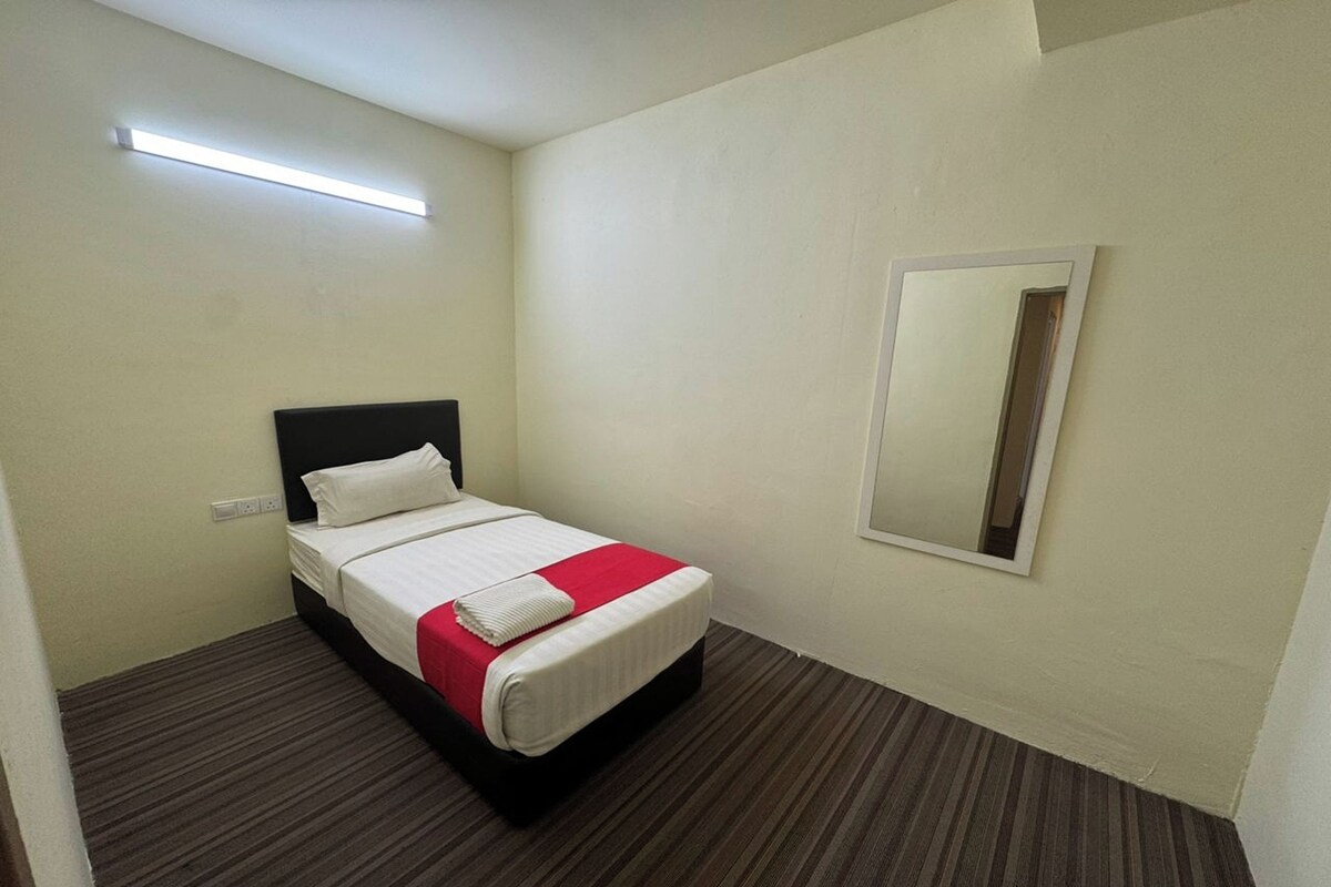 Quarto de hotel com uma cama de solteiro, uma mesinha de cabeceira, um espelho e um candeeiro.