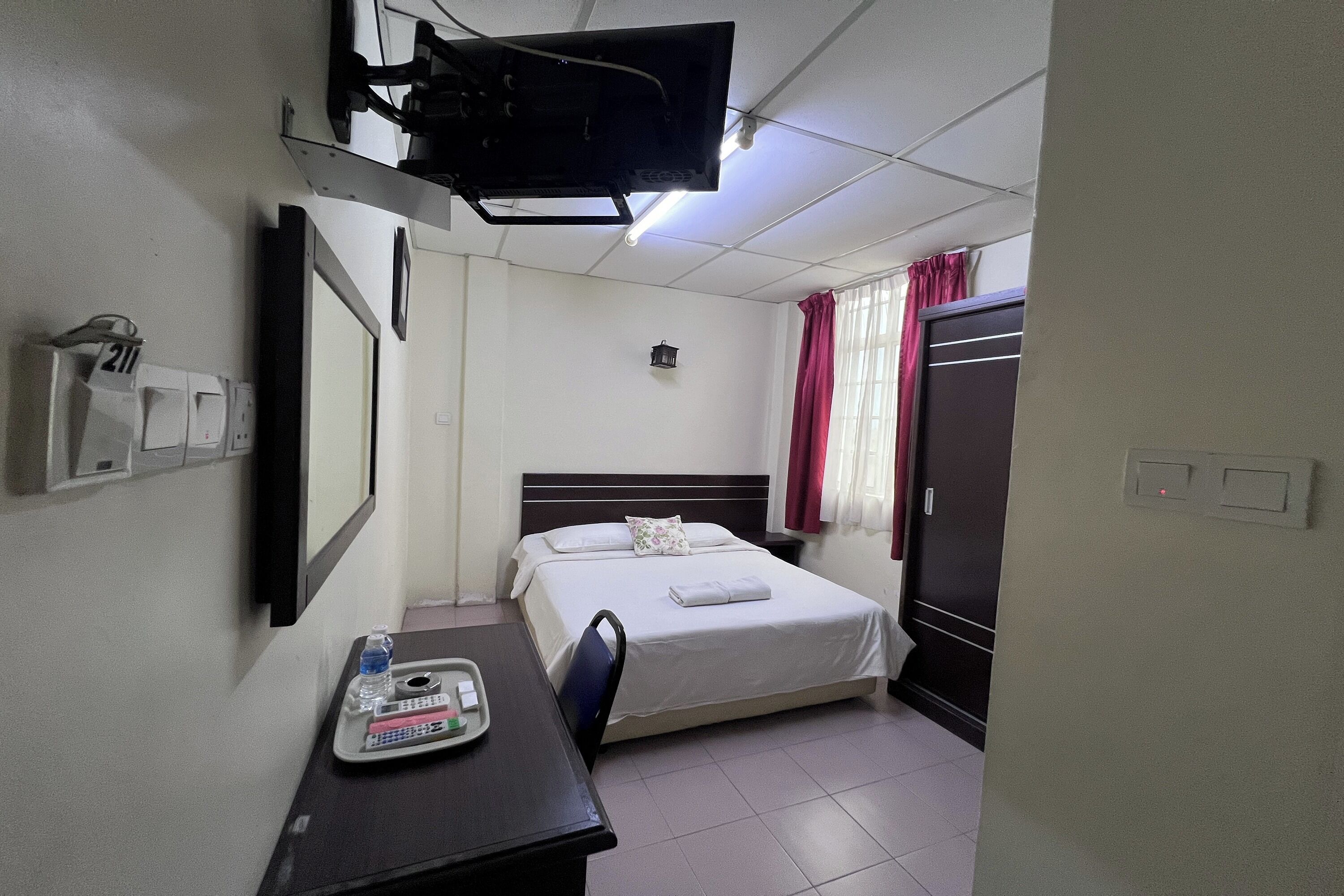 A hotel room with a bed, a desk with a tray of toiletries, a television mounted on the wall, and a wardrobe.