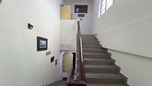 Una escalera con barandilla, un cartel que indica el camino a la sala "SURA" y una puerta al final.