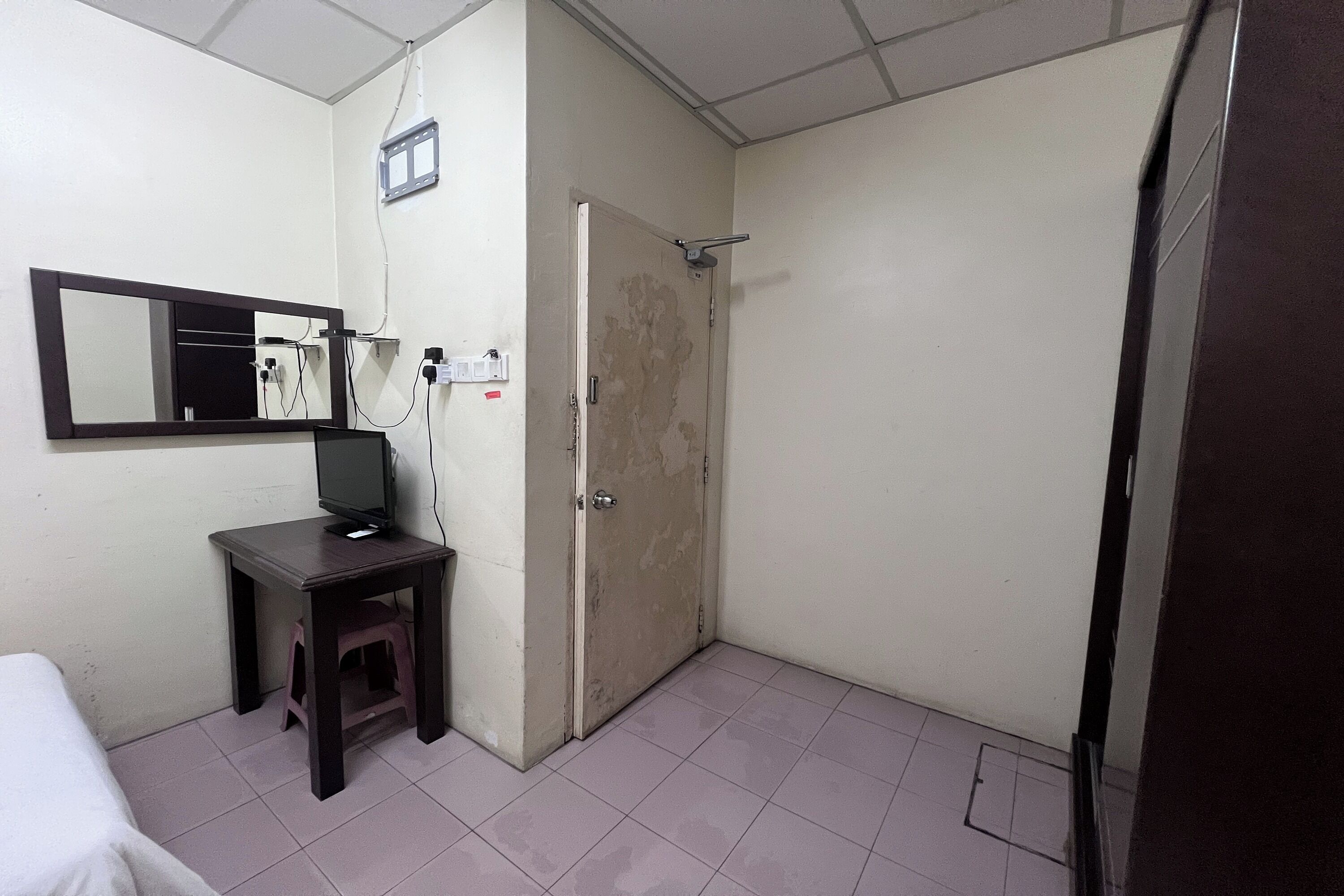 Una habitación pequeña con una cama, un escritorio con una computadora, un espejo y una puerta que da a un baño.