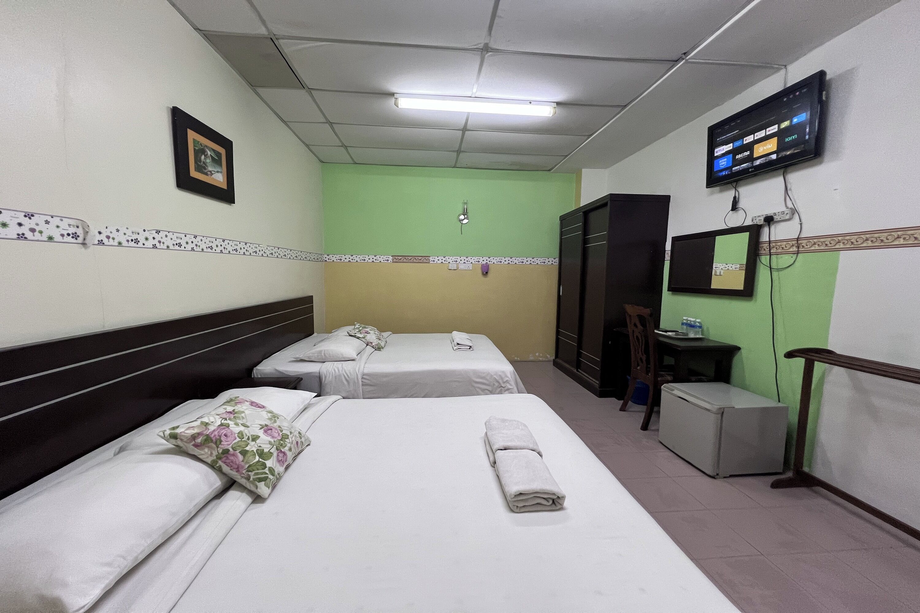Habitació d'hotel amb dos llits individuals, una televisió penjada a la paret, una taula petita amb una cadira i un frigorífic.