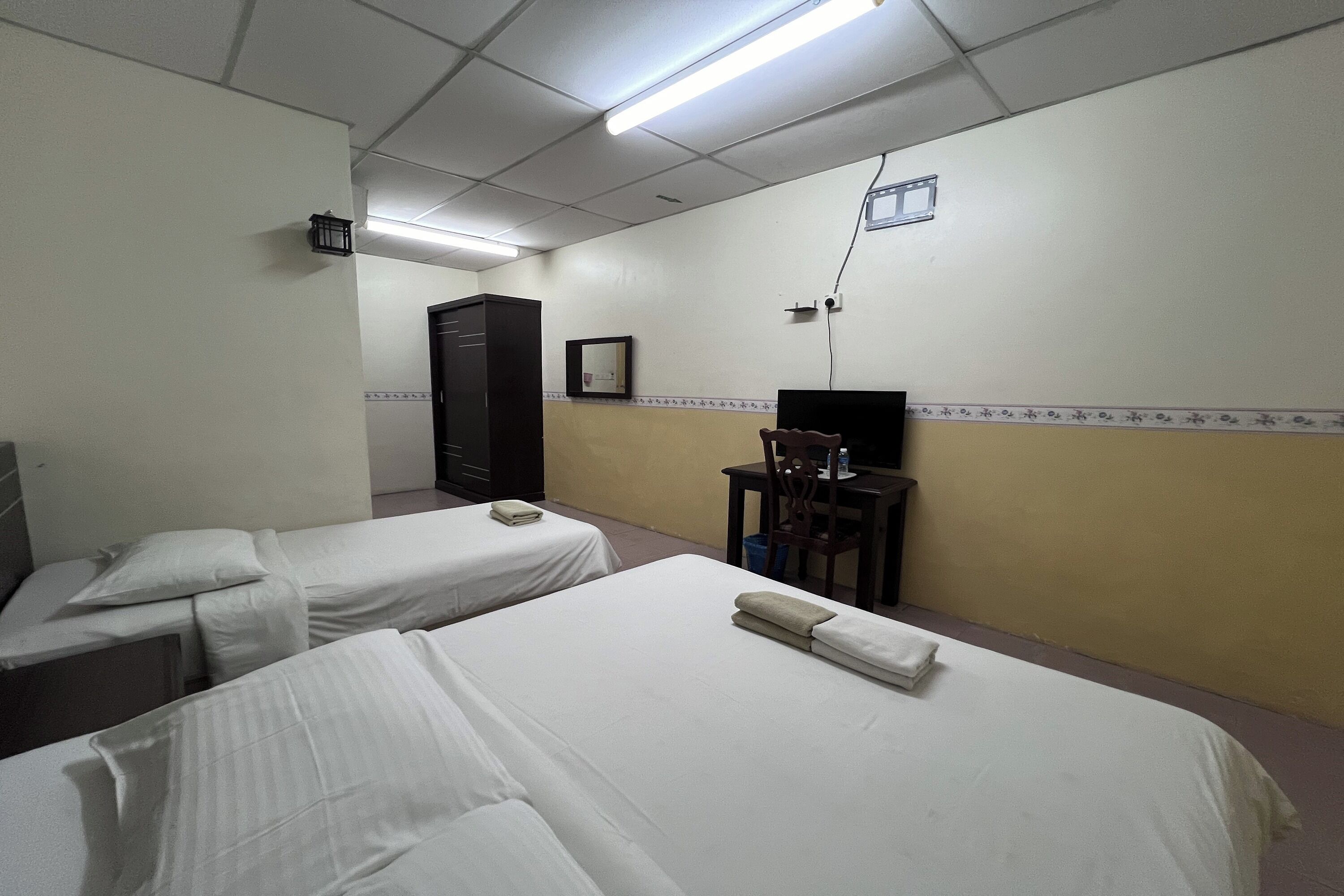 A hotel room with two single beds, a desk with a chair, a wardrobe, and a television.
