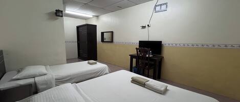 A hotel room with two single beds, a desk with a chair, a wardrobe, and a television.
