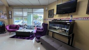 Un área de recepción con televisión, acuario, sillas moradas, un sofá y una mesa de centro.