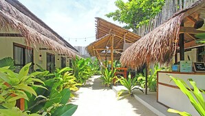 Een pad omgeven door gebouwen met rieten daken en weelderige begroeiing, wat doet denken aan een tropisch resort.