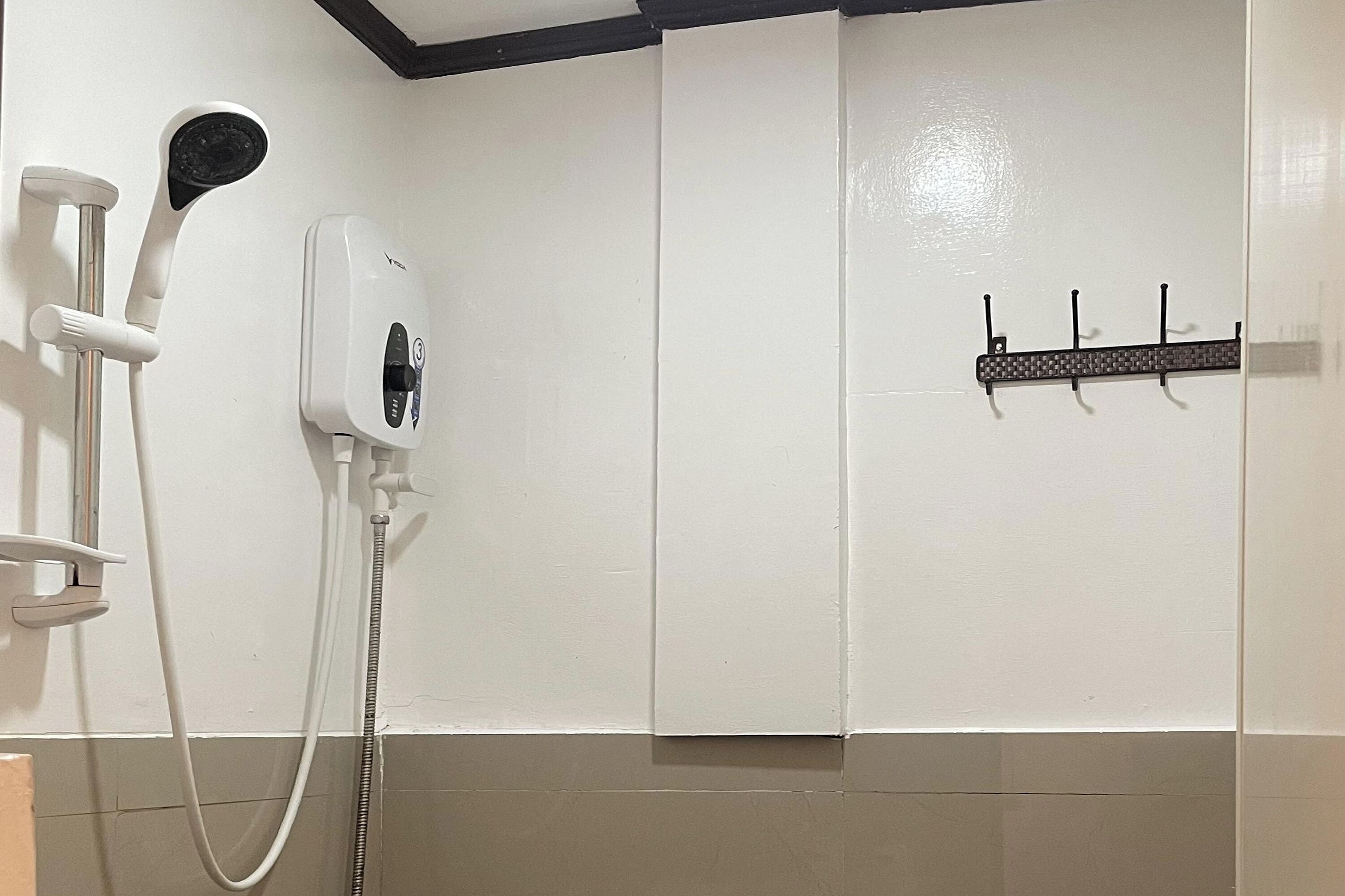 A bathroom with a white shower, a handheld showerhead, a wall-mounted hairdryer, and a towel rack.
