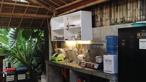 Een keuken met een bamboe plafond, witte planken, een waterdispenser en een zwarte koelkast.