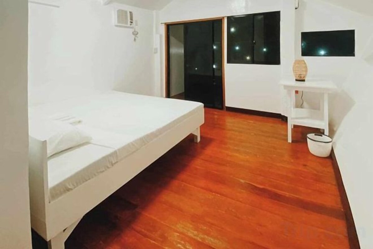 A room with a bed, a small table, a chair, and a window.